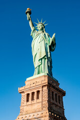 Fototapeta premium Low-angle full view of the Statue of Liberty standing on its pedestal under a clear blue sky on Liberty Island in New York Harbor, USA. 