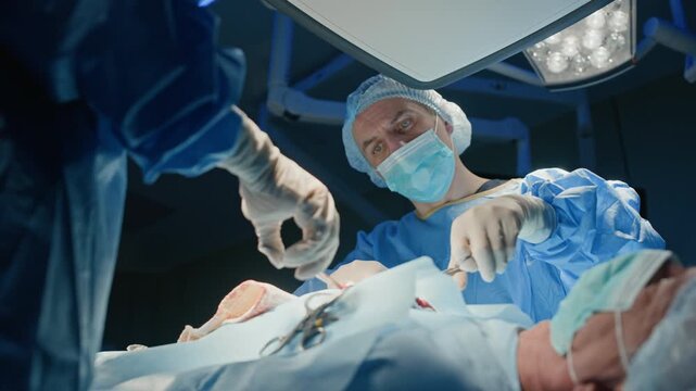 Low angle shot of two surgeon in sterile scrubs concentrated on operation on senior patient who lying on operating table