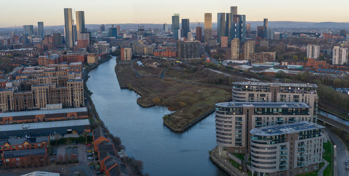 A wide aerial panorama capturing the Pomona Island development site, the River Irwell, and the dense skyscraper cluster in Manchester, England, UK.