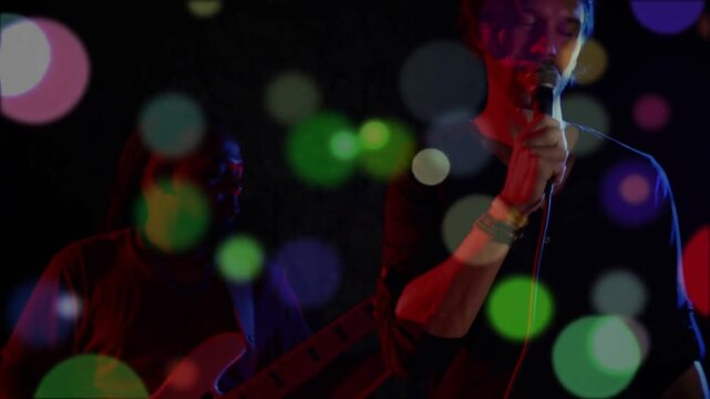 Bokeh pulsing lead singer moving adjusting mic, singing and engaging crowd bassist staying shadowed