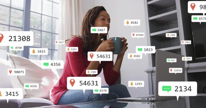 Woman holding blue mug and sipping while laptop getting business alerts, processing badges around