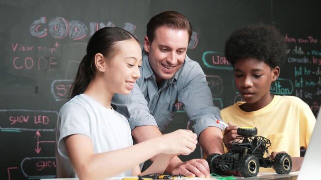 Caucasian teacher pointing at laptop screen while explain car model system at blackboard with coding or programming code written. Happy diverse student learning about robotic construction. Edification