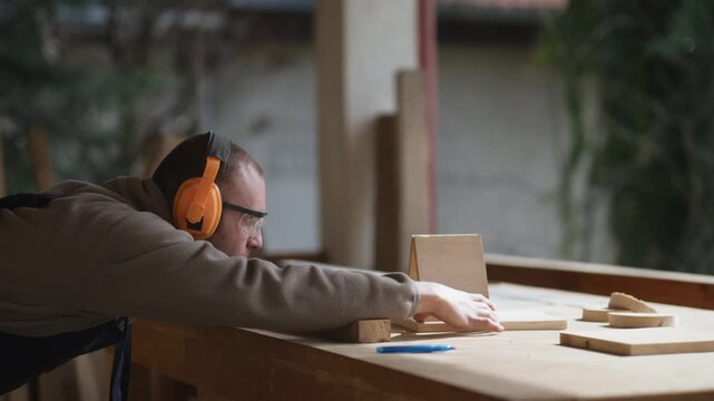 A focused woodworker in safety gear carefully cuts a piece of wood on a table saw. The craftsman demonstrates dedication and precision.