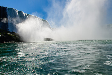 Obraz premium Lone rock stands amid rushing waters at foot of Horseshoe Falls, surrounded by thick vapor 