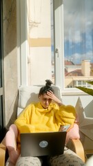 Fototapeta premium Relaxed Female Individual Engaging With Her Laptop On Sunny City Balcony With Plants And Skyline