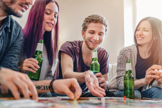 Group of young people playing a board game at home, drinking beer, sitting on couch, laughing, having fun, social interaction, indoor entertainment, leisure, friendship and weekend lifestyle concept