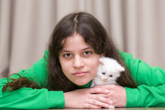 A teenage girl plays with a white kitten
