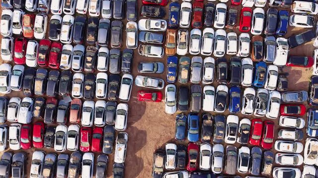 Top-down aerial of densely packed vehicles damaged by flooding, showing mud-covered roofs and salvage yard storage layout after extreme weather event