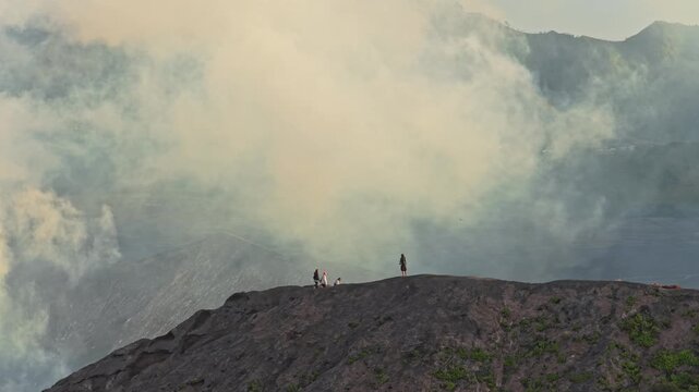 People on mount bromo crater rim with volcano smoke