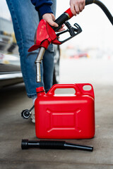 Fototapeta premium Gasoline flowing from fuel pump nozzle into red plastic canister.