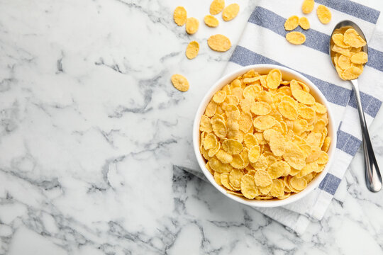 Tasty corn flakes in bowl and spoon on white marble table, flat lay. Space for text