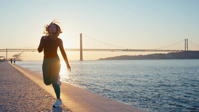 Athletic woman running on city embankment at sunset