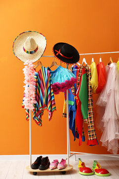 Different carnival clothes and accessories hanging on rack near orange wall indoors