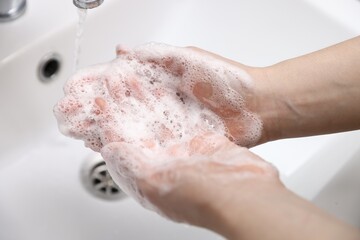 Fototapeta premium Woman washing hands with soap above white sink, closeup