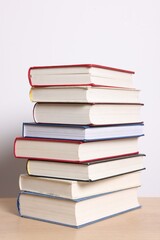 Fototapeta premium Stack of many books on wooden table against light background