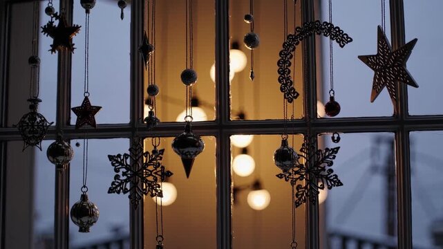 Warm window with hanging holiday ornaments, soft bokeh lights, dim chandelier glow, star and crescent baubles suspended against city silhouette through frosted glass, cozy evening mood for shop window