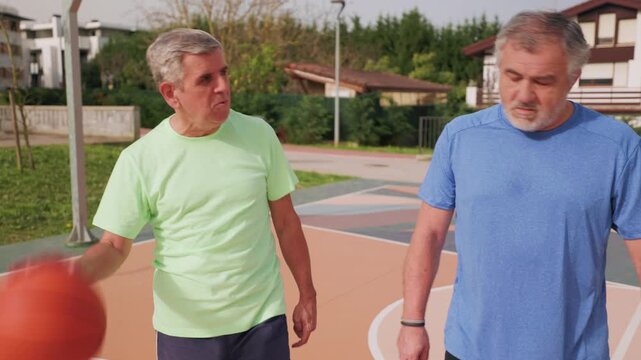 Two senior men enjoy their retirement playing basketball together on an outdoor court, embodying an active lifestyle and friendship through sport, promoting wellbeing and healthy aging