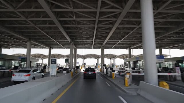 Driving through a multi-lane border checkpoint or toll plaza on a clear day, showcasing the modern infrastructure and organized flow of vehicles for entry or payment