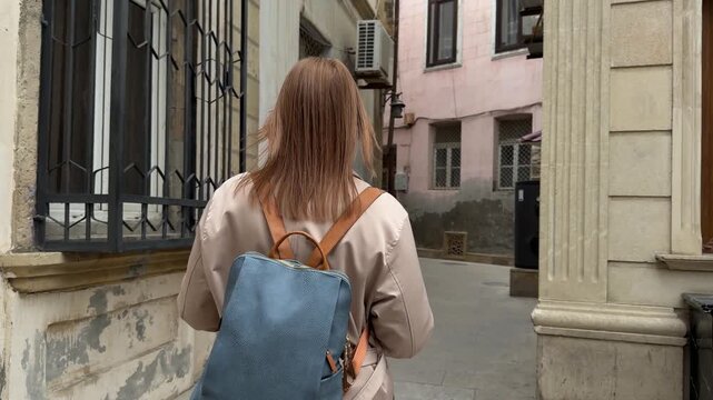 Back view of a female traveler walking through a narrow street in the old city of Baku, Azerbaijan, surrounded by aged stone walls and historic architecture, suitable for travel