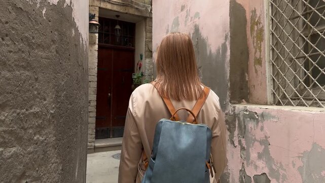 Back view of a female traveler walking through a narrow street in the old city of Baku, Azerbaijan, surrounded by aged stone walls and historic architecture, suitable for travel