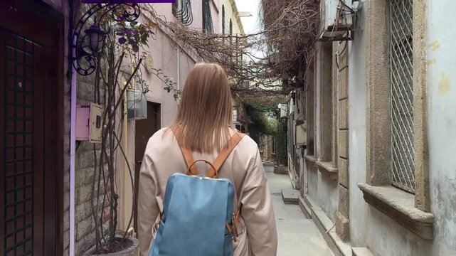 Back view of a female traveler walking through a narrow street in the old city of Baku, Azerbaijan, surrounded by aged stone walls and historic architecture, suitable for travel