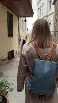 Back view of a female traveler walking through a narrow street in the old city of Baku, Azerbaijan, surrounded by aged stone walls and historic architecture, suitable for travel