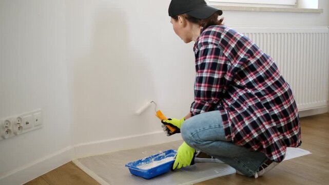 House Painter in Gloves holds a paint roller and painting a wall in a room during daylight hours
