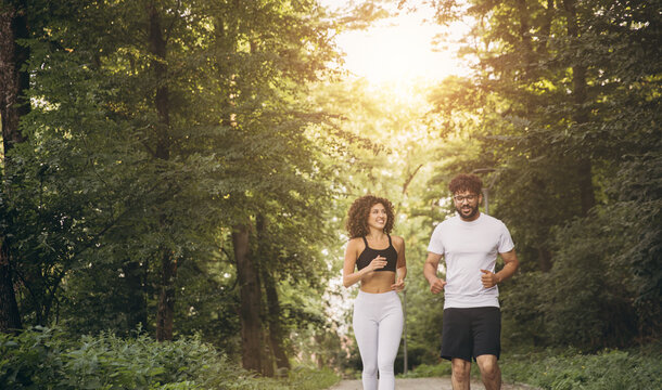 Diverse couple jogging on a path, staying active in a natural outdoor park setting during a sunny summer day