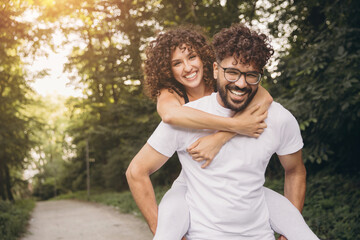 Fototapeta premium Happy diverse couple embracing a piggyback ride in a sunny park celebrating love and outdoor lifestyle