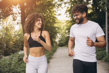 Obraz premium Happy couple jogging outdoors in a park, enjoying their fitness workout, smiling and exercising together