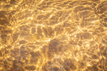 A clear stream of river water flows over a sandy-pebbly bottom on a sunny day. Sunlight creates golden wavy patterns on the surface and bottom of the reservoir. The water is shallow and has a warm gol © Alexei Vinnikov