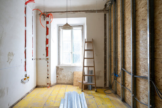 Interior renovation room with exposed wiring channels, unfinished walls and natural window light in residential construction project