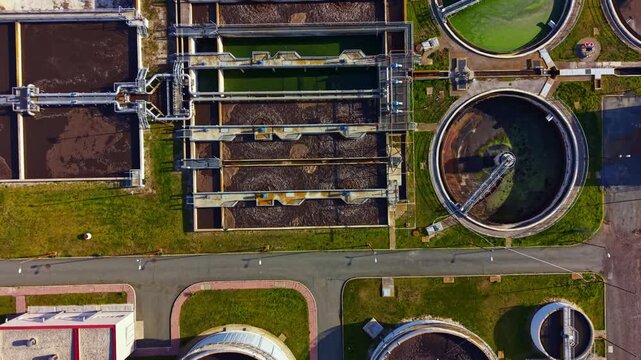 A wastewater treatment facility in a city. Various tanks and equipment are visible, with sections used for water purification. Activity is ongoing during daytime.