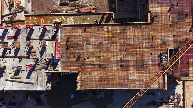 Workers are busy at a construction site, focusing on a large metal structure. Steel beams and rebar are arranged on the ground while machinery is in use.