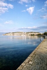 Obraz premium View of Lake Ohrid and the historic city of Ohrid in North Macedonia. A stone paved promenade is in the foreground next to calm blue water with sky reflections. Sunny daytime urban landscape view
