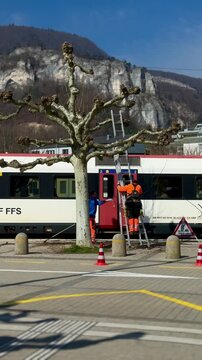 Railway workers performing maintenance near a stationary train at a railway station. Industrial scene with transport infrastructure, safety work and daily operations.