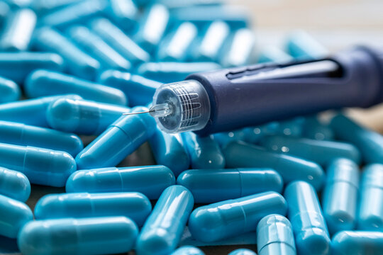 Close-up shot of a modern medical injection pen with a sharp needle resting on a large pile of bright blue pharmaceutical capsules, representing diverse options for diabetes and healthcare treatment