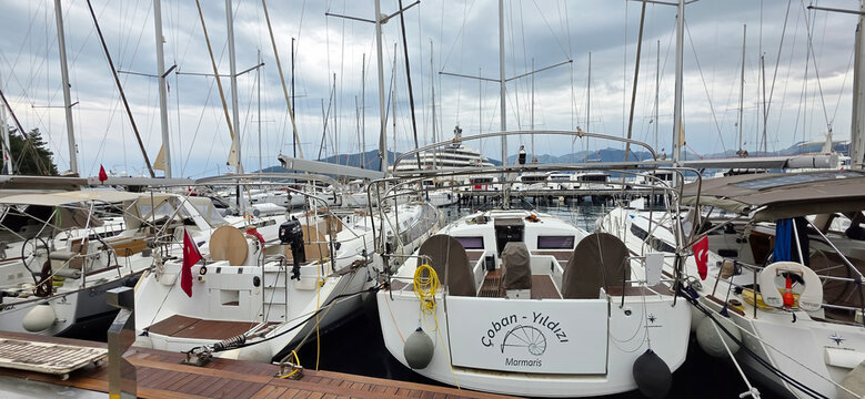 Sailboats docked at marina with cloudy sky and distant hills
