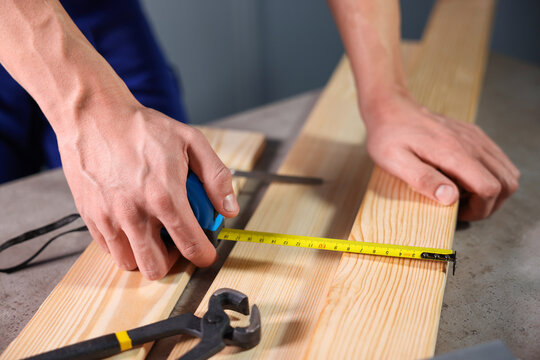 Man measuring wooden plank with tape at grey table, closeup