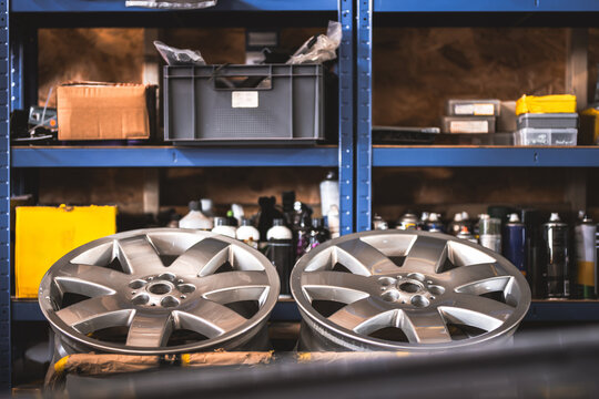 Two shiny alloy car wheels displayed in a workshop storage area