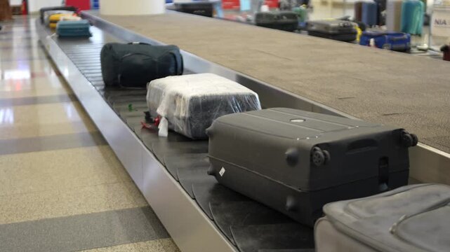 Suitcases moving on baggage conveyor belt at check-out area at arrival terminal in modern airport. Travel backpacks and suitcases moving around on luggage carousel in airport for passengers to pick up
