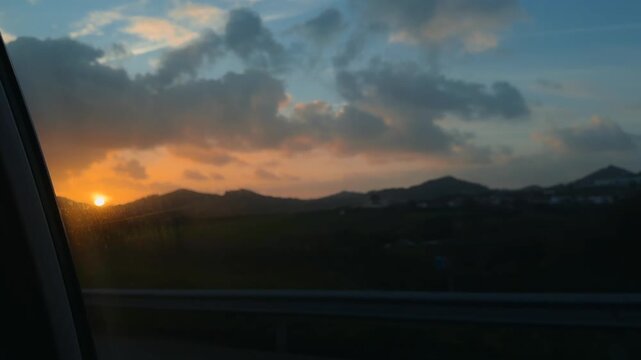 Car window captures sunset with distant hills and reflections