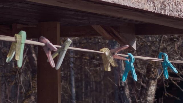 Weathered rope supports colorful clothespins. Rustic porch scene with soft autumn light and blurred background