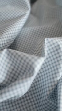 Close-up of soft blue and white gingham fabric texture with gentle folds and ripples. Classic checkered pattern textile background for fashion, home decor, and rustic themes.