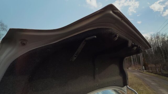 Open trunk with cloudy sky backdrop. Empty car trunk open on remote country road beneath overcast sky with visible bag inside