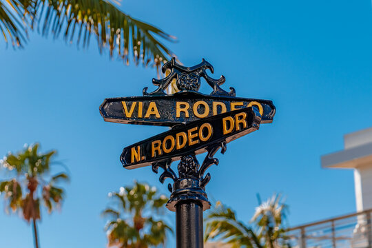Close-up view of the decorative Via Rodeo and North Rodeo Drive street sign with palm trees in the background in Beverly Hills, California, USA. Luxury shopping district, city landmark and travel 