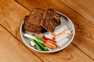 Rustic plate of sliced seeded rye bread with rolled cold cuts, spring onions, garlic and chili