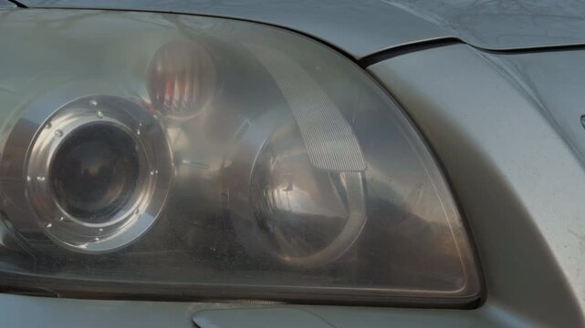 Reflections and scratches on lens. Closeup photograph emphasizing intricate details of car headlamp glass and chrome components