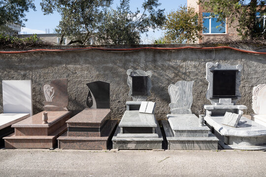 Gravestones and marble tombstones display at cemetery shop. Different designs and stone types including granite and marble. Funeral industry, memorial services and stone craftsmanship concept.