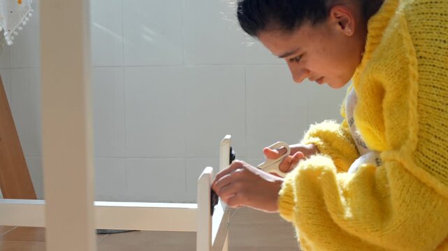 Woman Fixing Furniture. Lady Carefully Puts Together Wooden Stool Under Natural Morning Illumination